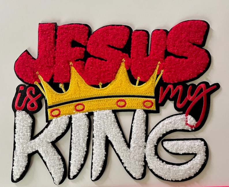 May include: Embroidered patch with the words "JESUS is my KING" in red, white, and black. A yellow and red crown is centered between "JESUS" and "KING". The patch has a textured, fuzzy appearance.