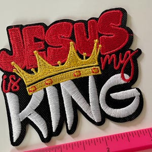 May include: Embroidered patch with the words "JESUS is my KING" in red and white thread. A gold crown with red accents sits above the word "KING". The patch has a black border.