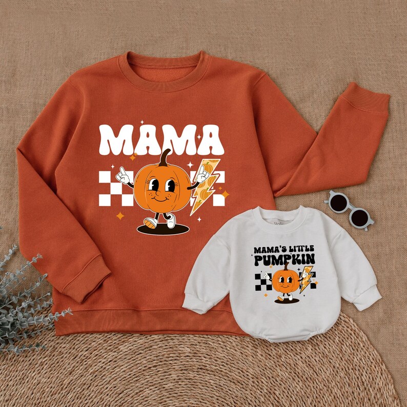 May include: Orange sweatshirt with the text "MAMA" and a cartoon pumpkin holding a lightning bolt. White onesie with the text "MAMA'S LITTLE PUMPKIN" and a cartoon pumpkin holding a lightning bolt.