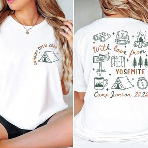 May include: A white t-shirt featuring a small tent graphic and the text Camping Crew 2026 on the front left chest. The back displays a collection of camping icons including binoculars, a backpack, a campfire, a map, trees, a mug, and a tent with the text With love from YOSEMITE Camp Jonson 2026.