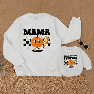 May include: White sweatshirts with a pumpkin graphic and text. The larger sweatshirt says "MAMA" and the smaller sweatshirt says "MAMA'S LITTLE PUMPKIN".