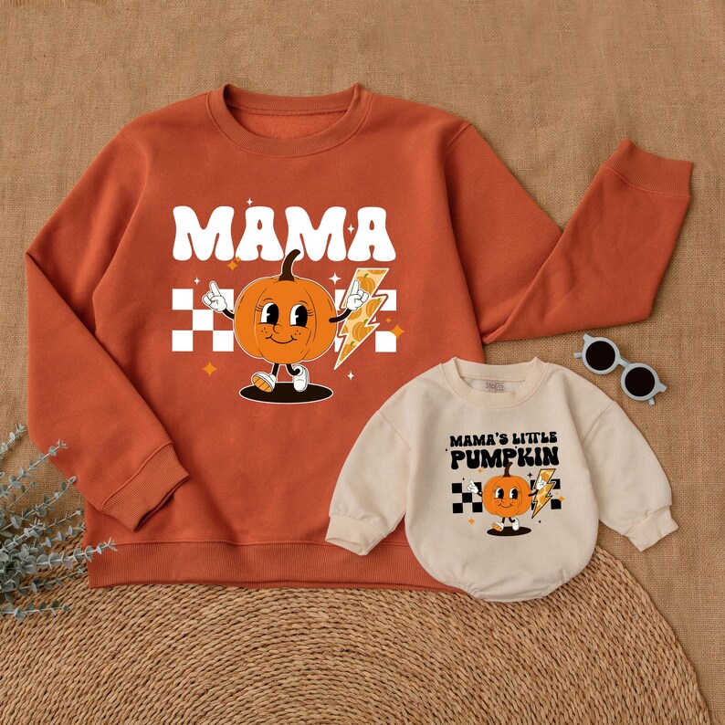 May include: A matching set of orange sweatshirts with a pumpkin graphic. The larger sweatshirt says "MAMA" and the smaller sweatshirt says "MAMA'S LITTLE PUMPKIN".