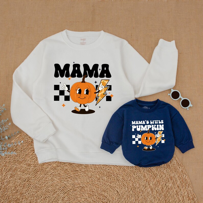 May include: A white sweatshirt with the text "MAMA" and a cartoon pumpkin holding a lightning bolt. A matching blue sweatshirt with the text "MAMA'S LITTLE PUMPKIN" and a cartoon pumpkin holding a lightning bolt.