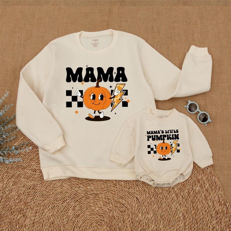 May include: A set of two cream-colored sweatshirts with a pumpkin graphic. The larger sweatshirt says "Mama" and the smaller sweatshirt says "Mama's Little Pumpkin".