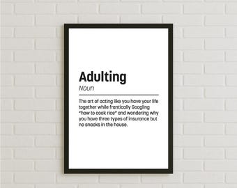 May include: A framed print with the definition of "Adulting." The black frame surrounds a white background with the word "Adulting" in bold black letters, followed by a definition that includes Googling "how to cook rice."
