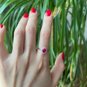 May include: A silver ring with a red oval gemstone surrounded by smaller white gemstones.