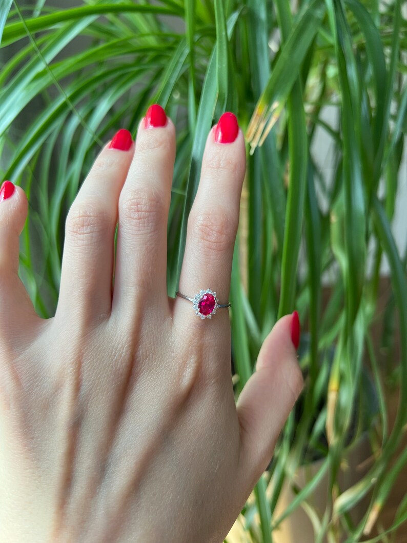 May include: A silver ring with a red oval gemstone surrounded by smaller white gemstones.