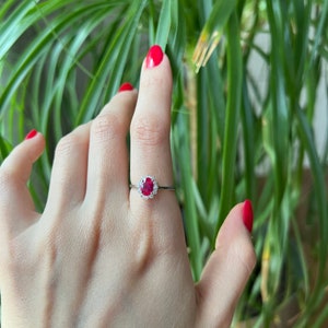 May include: A silver ring with a red oval gemstone surrounded by smaller white gemstones.