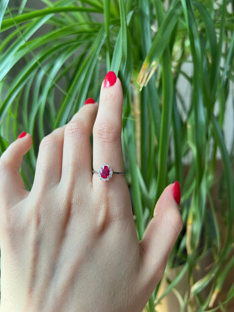 May include: A silver ring with a red oval gemstone surrounded by smaller white gemstones.
