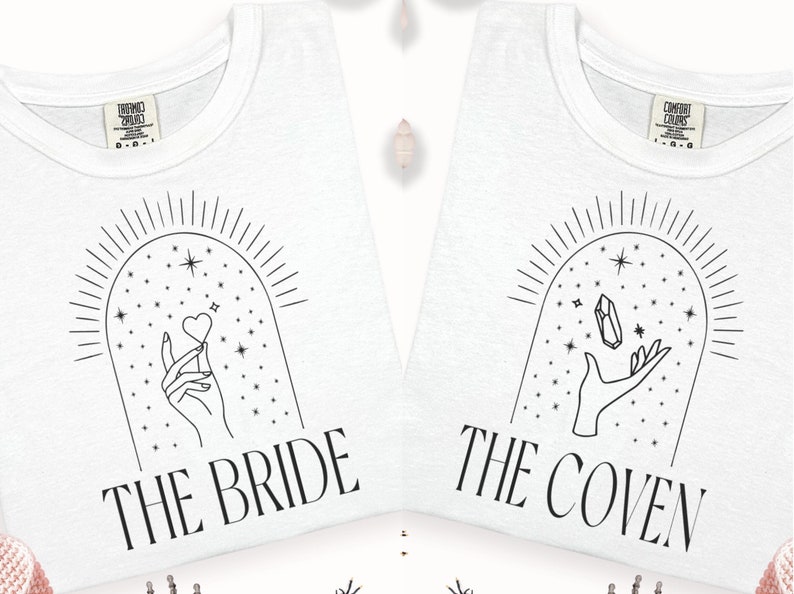 May include: Two white t-shirts with black line drawings of hands holding a heart and a crystal. The text "The Bride" and "The Coven" are printed on the shirts.
