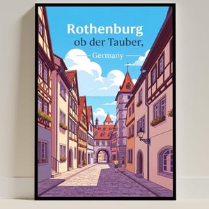 May include: A framed art print featuring a street scene in Rothenburg ob der Tauber, Germany. The artwork shows a cobbled street flanked by buildings in various colours, under a blue sky. The text "Rothenburg ob der Tauber, Germany" is at the top.