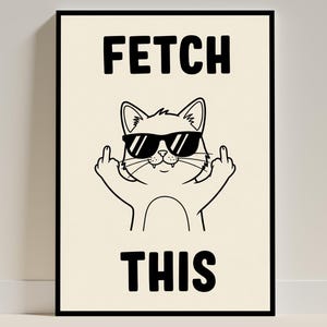 May include: Black framed art print featuring a cartoon cat wearing sunglasses and giving the middle fingers. The words "FETCH THIS" are printed in bold, black capital letters above and below the cat illustration. The background is a light beige color.