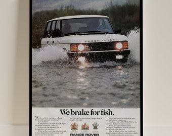 Puede incluir: Un Range Rover blanco conduce a través de un cuerpo de agua poco profundo. El coche tiene un parachoques negro y molduras negras alrededor de las ventanas. El texto "We brake for fish." está impreso debajo del coche. El texto "Range Rover" está impreso debajo del texto "We brake for fish."