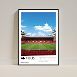 以下が含まれることがあります： リバプールFCの本拠地であるアンフィールドスタジアムの額入りポスター。画像には、スタジアムの緑のフィールド、赤い座席、青い空が写っています。「ANFIELD」の文字が太字の白い文字で表示されています。
