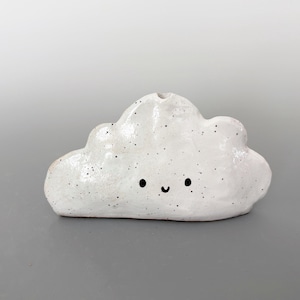 Könnte beinhalten: Eine weiße Keramikvase in Wolkenform mit einem lächelnden Gesicht. Die Vase hat eine gesprenkelte Textur und eine kleine Öffnung oben. Die Wolke ist etwa 13 cm lang.