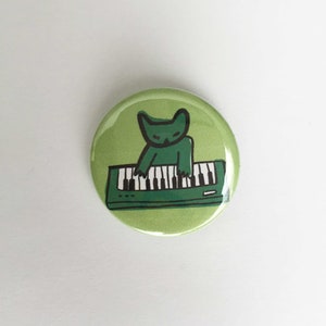 Pode incluir: Botão verde com um gato verde tocando um teclado. O teclado é verde com teclas pretas.