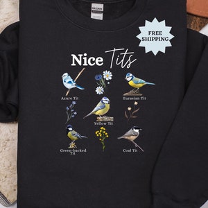 Pode incluir: Camisola preta com o texto "Nice Tits" e ilustrações de diferentes tipos de pássaros com os seus nomes: Chapim-azul, Chapim-verde, Chapim-real, Chapim-preto e Chapim-azul.