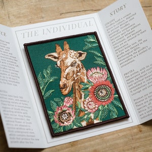 May include: A green embroidered patch featuring a giraffe with a brown and white patterned coat, surrounded by pink and green flowers. The patch has a brown border and the text "THE INDIVIDUAL" is printed above the image.