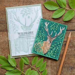 May include: A green embroidered patch featuring a red deer with antlers standing in a forest setting. The patch has the text "WILDLORE EMBROIDERED GALLERY PATCH" with the tagline "With The Science & Story Behind Each Species".