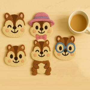 May include: A collection of five chipmunk-shaped coasters, each with a smiling face and rosy cheeks. One chipmunk wears a pink hat and bow tie, another has blue glasses. A white mug of coffee sits nearby. The coasters are made of a textured, light-colored material.