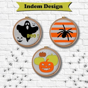 Puede incluir: Tres aros de bordado con temática de Halloween. Uno presenta un fantasma negro con el texto "BOO!", otro una araña negra sobre rayas naranjas y el último una calabaza con calabazas. El fondo es una pared de ladrillos blancos con ilustraciones de arañas.