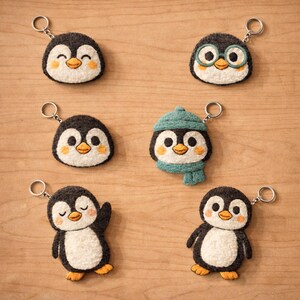 May include: A selection of handmade penguin keyrings. Each keyring features a black and white penguin design with orange feet and a yellow beak. Some penguins have accessories like glasses, a hat, and a scarf. The keyrings are on a wooden surface.