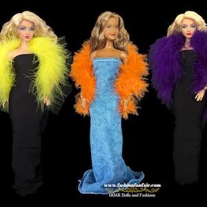 Puede incluir: Tres muñecas de moda que llevan boas de plumas de diferentes colores. Las muñecas llevan vestidos negros, azules y negros. Las boas son amarillas, naranjas y moradas.