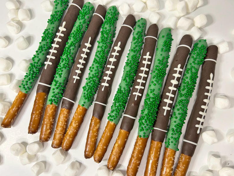May include: Pretzel rods dipped in chocolate and decorated to resemble footballs. The pretzels have a brown chocolate coating with white laces and green sprinkles. A fun treat for game day or a sports-themed party.