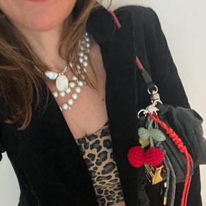 May include: A black velvet blazer with a leopard print top and a multi-strand pearl necklace. A small black bag with red cherry and green leaf charms hangs from the blazer.