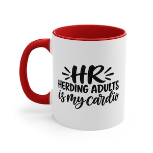 May include: A white ceramic mug with a bright red handle and interior rim. The front features black text that reads HR HERDING ADULTS IS MY CARDIO, with decorative lines above and below the letters HR, presented in a bold, stylised font.