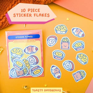 May include: A collection of 10 sticker flakes depicting pastries such as croissants and buns. The stickers are water-resistant and long-lasting, with the text "TOASTY DAYDREAMS" and "STICKER FLAKES" on the packaging. The background is a warm orange.