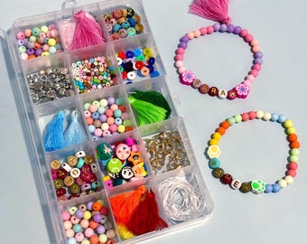 May include: A clear plastic storage box filled with colorful beads, letters, and charms. Two bracelets are made with the beads, one says "SARAH" and the other says "JAMES".