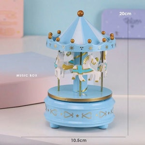 May include: A blue and white carousel music box with gold accents and four white horses. The music box is 10.5 cm in diameter and 20 cm tall.