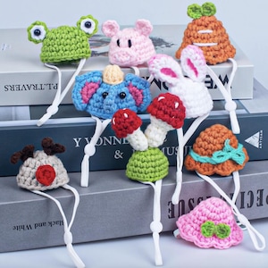 Op de afbeelding: Een set van tien kleurrijke gehaakte dierenmutsen met elastische bandjes. De mutsen hebben verschillende dierenontwerpen, waaronder een kikker, een varken, een konijn, een olifant, een paddenstoel en een zonnehoed.