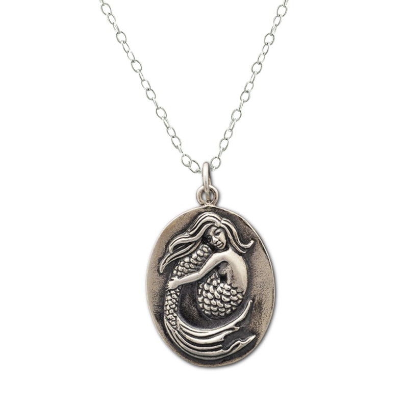 Make a Splash with an Oval Mermaid Charm Necklace in Sterling Silver. Solid sterling silver oval shaped mermaid pendant on sterling silver chain white background. Detailed mermaid with long hair in fetal position holding her legs.