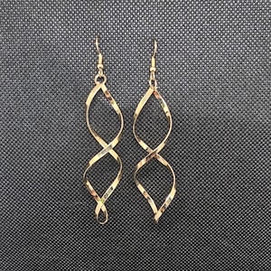 Könnte beinhalten: Ein Paar goldfarbene Ohrringe mit einem gedrehten, spiralförmigen Design. Die Ohrringe sind lang und hängen herunter.