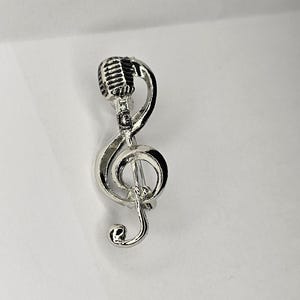 Könnte beinhalten: Silberne Violinschlüssel-Musiknote mit Mikrofon-Design.