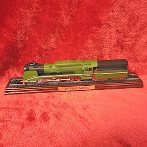 Könnte beinhalten: Ein Modellzug, DR 18201 Pacific, in Olivgrün, Schwarz und Rot, steht auf einem Holzsockel mit Gleisen. Der Modellzug ist eine detaillierte Nachbildung einer klassischen Lokomotive. Der Sockel hat ein kleines Schild mit dem Namen des Zuges.