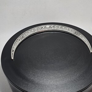 Puede incluir: Un plato redondo negro con un dise&ntilde;o de media luna plateada alrededor del borde. La luna tiene una superficie texturizada y presenta una serie de peque&ntilde;os c&iacute;rculos.