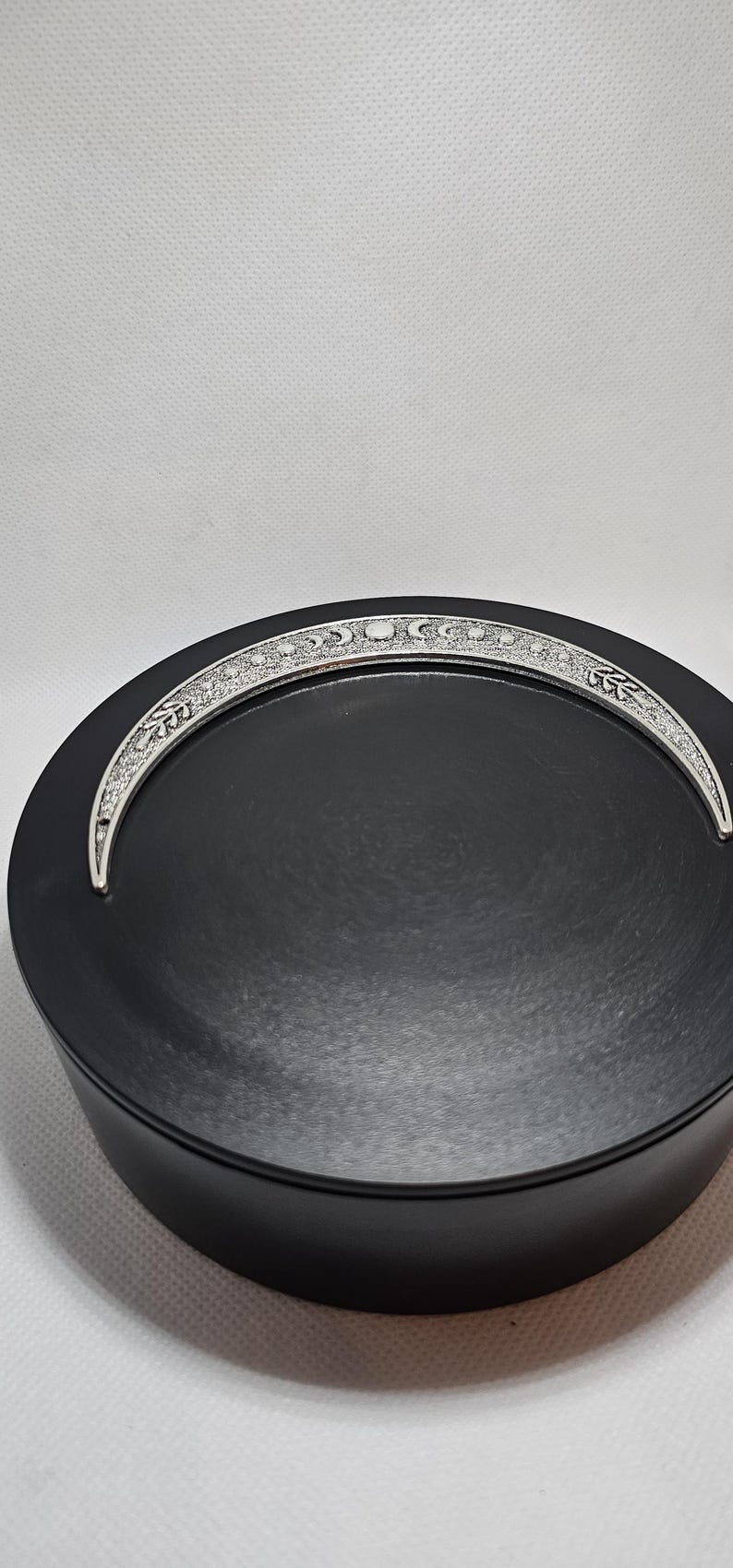 Puede incluir: Un plato redondo negro con un dise&ntilde;o de media luna plateada alrededor del borde. La luna tiene una superficie texturizada y presenta una serie de peque&ntilde;os c&iacute;rculos.