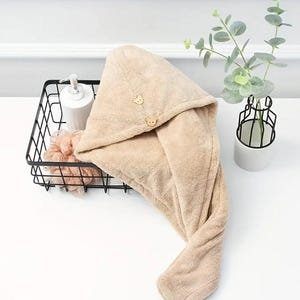 May include: A beige microfiber hair towel with a button closure. The towel is designed to wrap around the head and absorb moisture after showering.