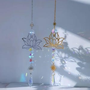 May include: Two gold-toned metal lotus flower suncatchers with iridescent crystal beads and teardrop-shaped prisms hanging from them.