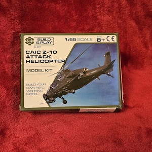 Könnte beinhalten: Modellbausatz für einen CAIC Z-10 Kampfhubschrauber. Die Box ist grün und schwarz mit dem Hubschrauberbild und dem Text "BUILD & PLAY" und "MODEL KIT". Der Maßstab ist 1:65.