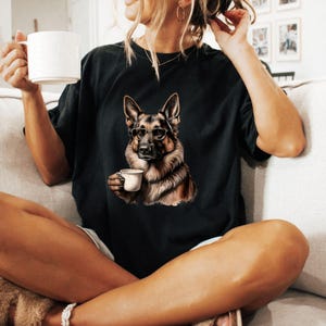 Puede incluir: Una camiseta negra con un gr&aacute;fico de un perro pastor alem&aacute;n con gafas y sosteniendo una taza de caf&eacute;.