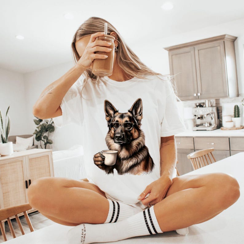 Puede incluir: Una camiseta blanca con un gr&aacute;fico de un perro pastor alem&aacute;n con gafas y sosteniendo una taza de caf&eacute;.