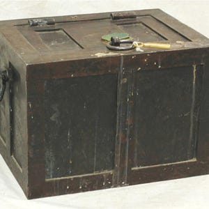 May include: A rectangular dark brown wooden chest featuring a hinged lid with a metal ring handle and a small brass-colored key resting on top. The sides of the chest are paneled and include large black metal ring handles on the exterior ends.