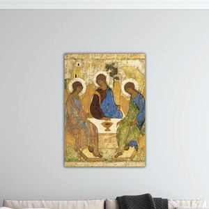 May include: A framed religious icon featuring three figures with halos, seated around a table. The figures are depicted in traditional robes of blue, red, and green hues. The background is a textured, aged gold.