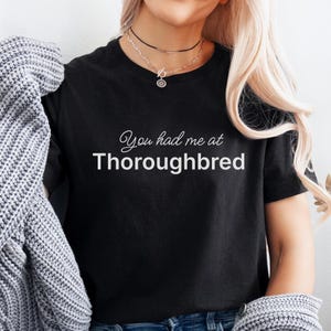 May include: Black t-shirt with the text "You had me at Thoroughbred" in white.