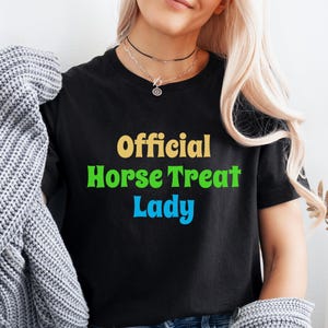 May include: A black t-shirt with the text "Official Horse Treat Lady" in colorful letters. The text is in a retro font style.