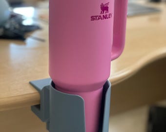 May include: A pink Stanley travel mug with a straw and lid, held in a gray cup holder.